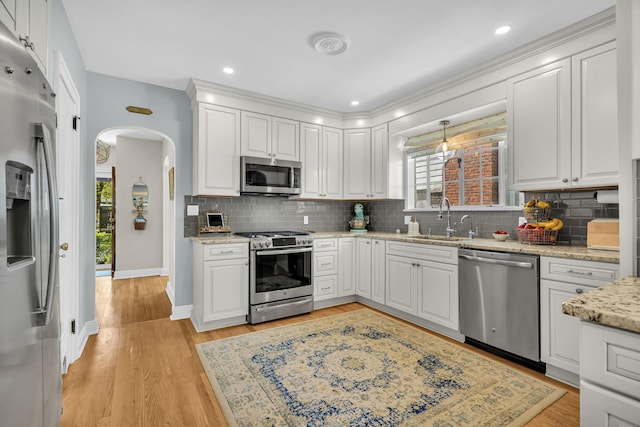kitchen with decorative backsplash, appliances with stainless steel finishes, arched walkways, a sink, and white cabinets