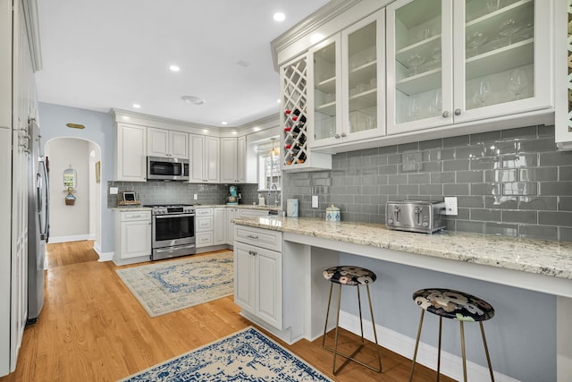 kitchen featuring a kitchen bar, appliances with stainless steel finishes, tasteful backsplash, arched walkways, and white cabinetry