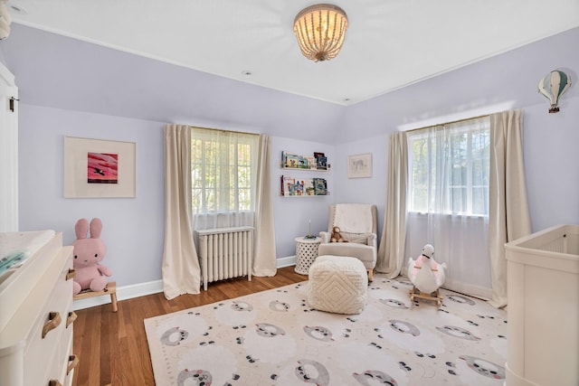 bedroom with radiator heating unit, baseboards, multiple windows, and wood finished floors