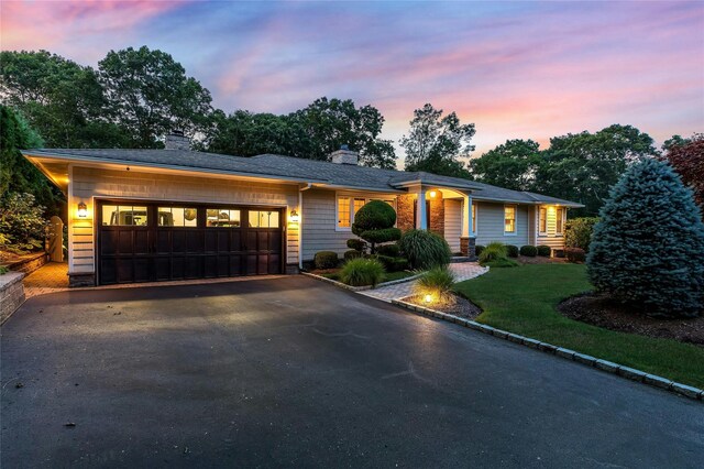 view of front of home featuring a chimney, aphalt driveway, a yard, and a garage