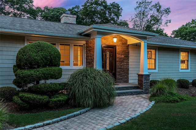 exterior entry at dusk with a shingled roof and a chimney