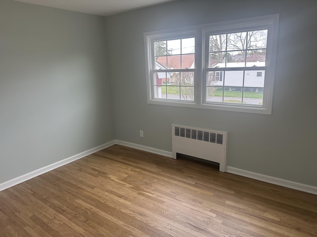unfurnished room featuring baseboards, radiator heating unit, and light wood finished floors