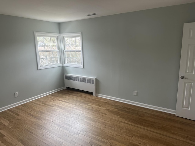 empty room with baseboards, wood finished floors, visible vents, and radiator