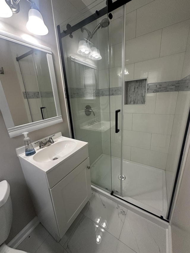 bathroom with a stall shower, toilet, baseboards, marble finish floor, and vanity