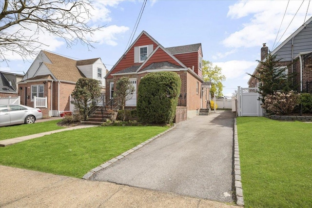 view of front of home with fence, a front lawn, aphalt driveway, brick siding, and a gate