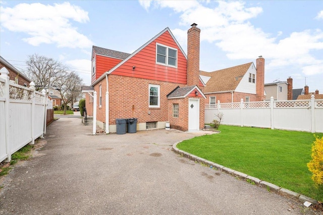 back of property featuring fence, a chimney, a yard, and brick siding