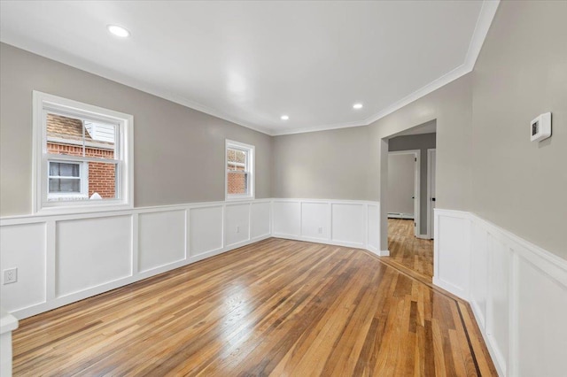 unfurnished room with crown molding, wainscoting, light wood-type flooring, a decorative wall, and recessed lighting