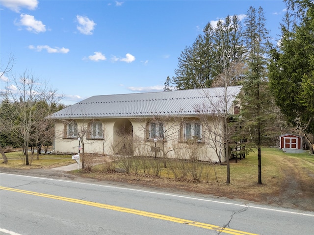 view of front of house featuring a front lawn, stucco siding, a shed, an outdoor structure, and metal roof