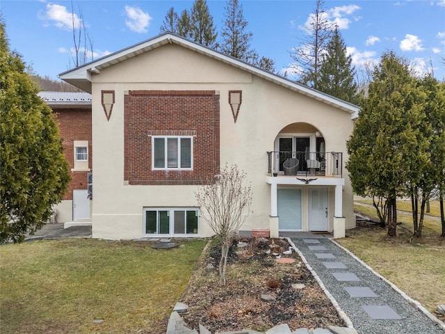 back of house with stucco siding, brick siding, a yard, and a balcony