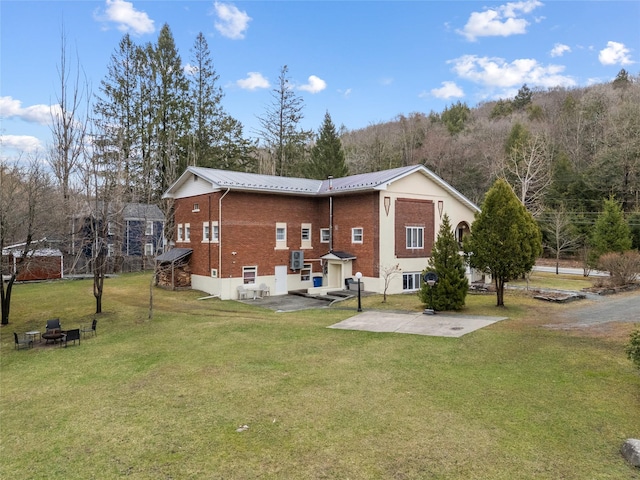 view of side of home featuring a patio area, a lawn, a fire pit, brick siding, and metal roof