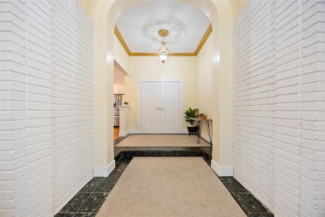 hallway with brick wall, baseboards, arched walkways, and ornamental molding