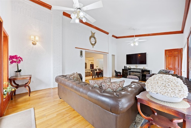 living room with a towering ceiling, wood finished floors, crown molding, and ceiling fan