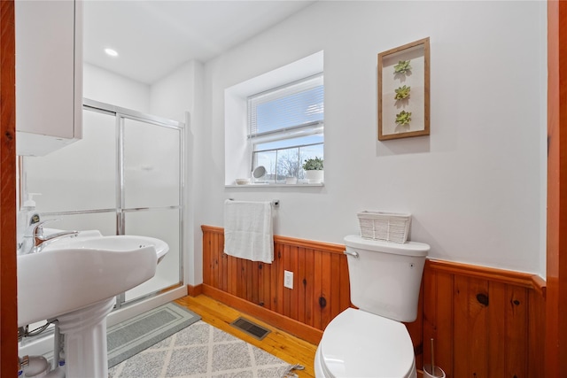 bathroom with a shower stall, toilet, wainscoting, wood walls, and visible vents