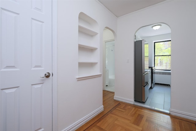 hall with built in shelves, crown molding, arched walkways, and baseboards