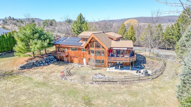 back of house with fence, solar panels, a wooden deck, a patio, and a lawn
