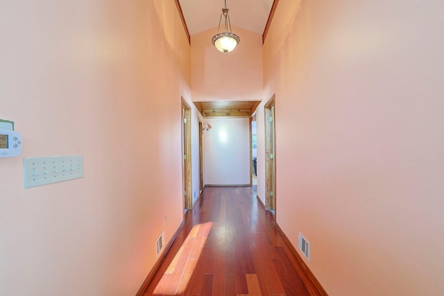 hallway with wood finished floors, a high ceiling, baseboards, and visible vents