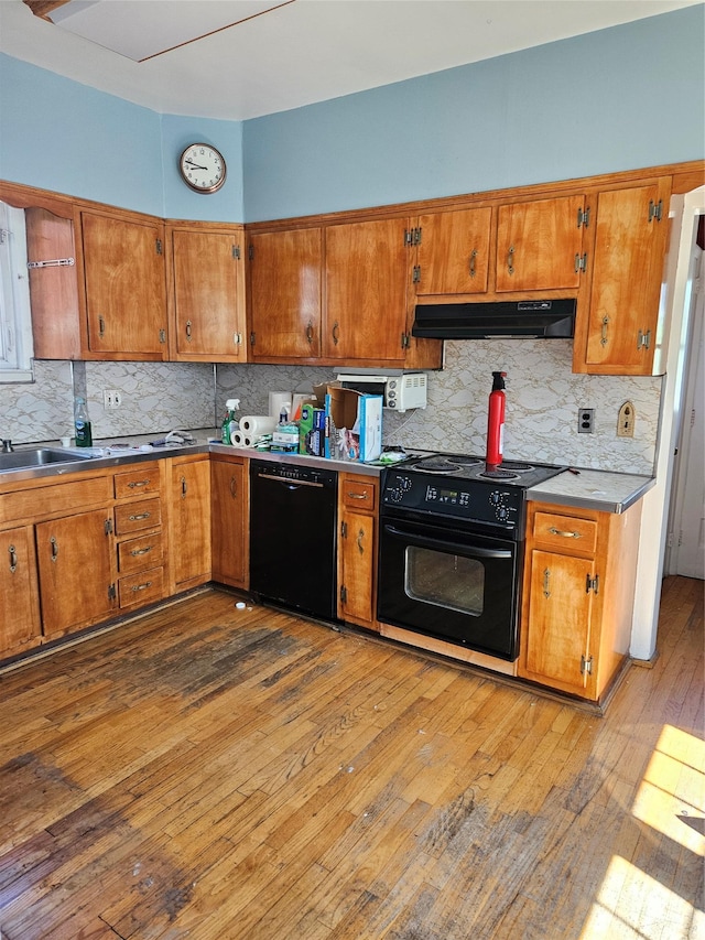 182 Parkway N, Yonkers, NY 10704 - kitchen with brown cabinetry, hardwood / wood-style flooring, under cabinet range hood, and black appliances