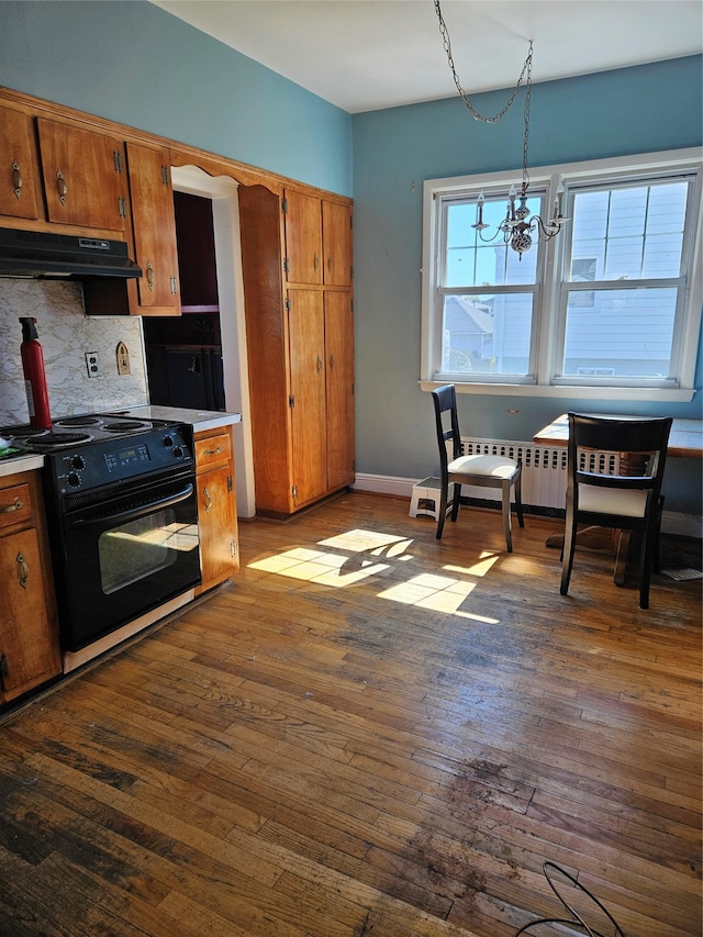 182 Parkway N, Yonkers, NY 10704 - kitchen with tasteful backsplash, brown cabinetry, black / electric stove, an inviting chandelier, and under cabinet range hood