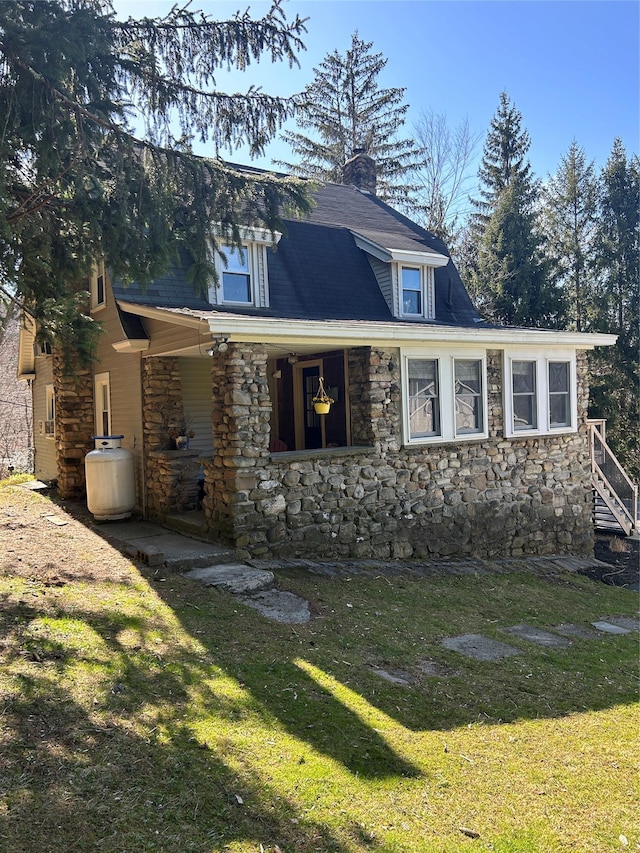 view of front of house with a front yard, stone siding, a chimney, and covered porch