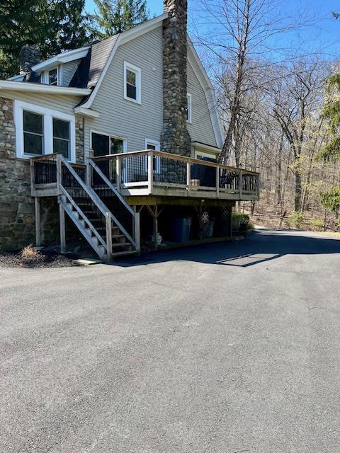 rear view of property with stone siding, a chimney, a wooden deck, a gambrel roof, and stairway