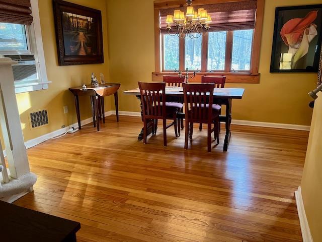 dining room with light wood-type flooring, baseboards, visible vents, and an inviting chandelier