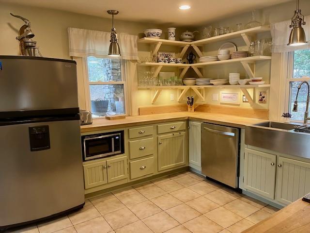 kitchen with appliances with stainless steel finishes, open shelves, hanging light fixtures, and light tile patterned floors