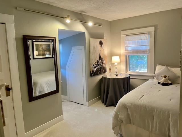 bedroom with light carpet, baseboards, and a textured ceiling