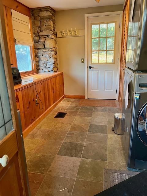entryway featuring stone finish floor, visible vents, and stacked washing maching and dryer