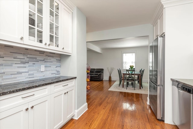 kitchen with glass insert cabinets, appliances with stainless steel finishes, tasteful backsplash, and white cabinets