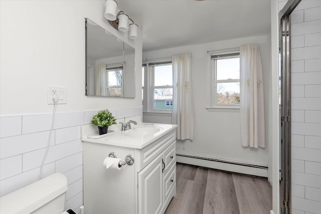 bathroom with vanity, wood finished floors, toilet, tile walls, and a baseboard heating unit
