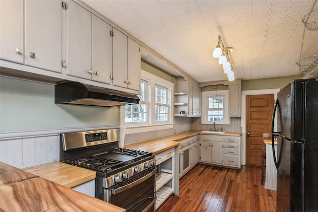 kitchen with a sink, freestanding refrigerator, gas stove, butcher block counters, and under cabinet range hood