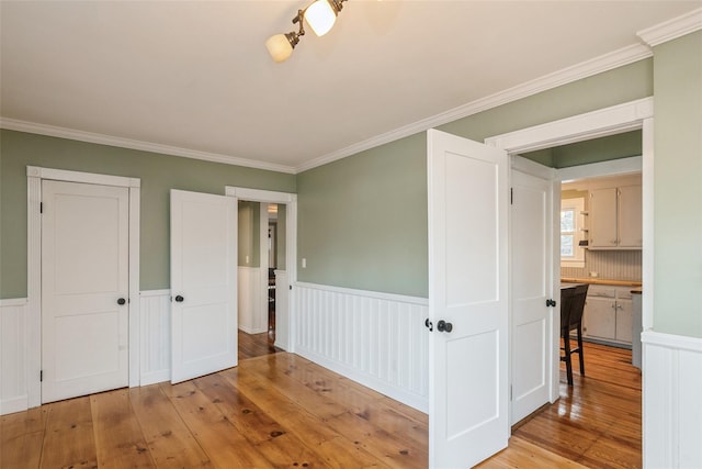 interior space with wainscoting, ornamental molding, and light wood-style flooring