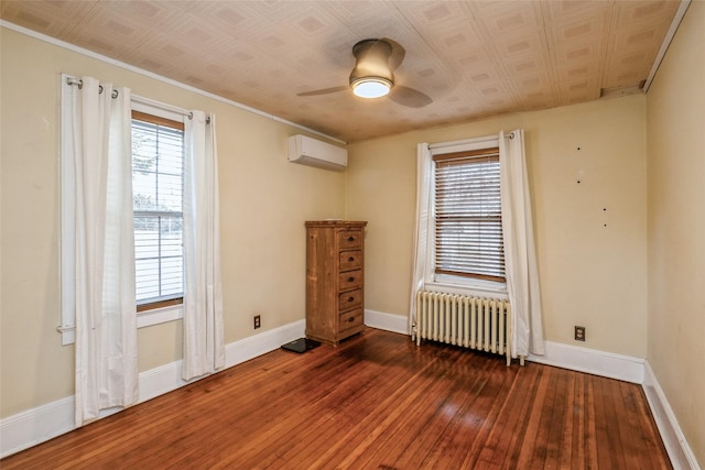 empty room with a wall mounted air conditioner, radiator heating unit, hardwood / wood-style flooring, ceiling fan, and baseboards