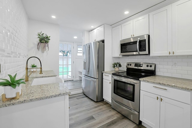 286 9th St, Verplanck, NY 10596 - kitchen featuring appliances with stainless steel finishes, a sink, decorative backsplash, light wood-style floors, and white cabinetry
