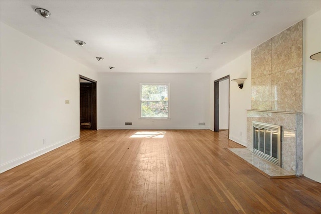 unfurnished living room with light wood-type flooring, a tiled fireplace, baseboards, and visible vents