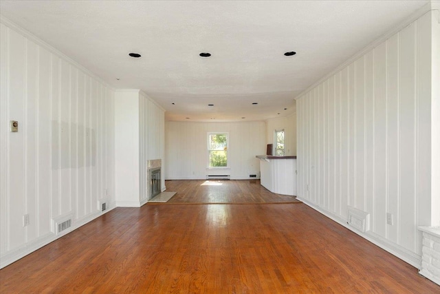 unfurnished living room with wood finished floors, visible vents, a baseboard heating unit, crown molding, and a fireplace
