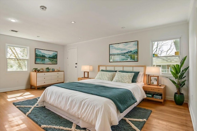 bedroom featuring baseboards, ornamental molding, multiple windows, and light wood-style floors