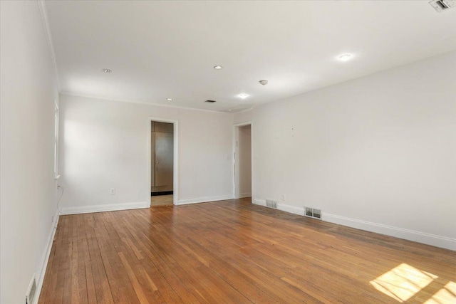spare room with hardwood / wood-style floors, visible vents, and baseboards