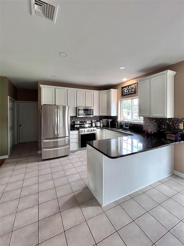 kitchen with a sink, stainless steel appliances, backsplash, a peninsula, and dark countertops
