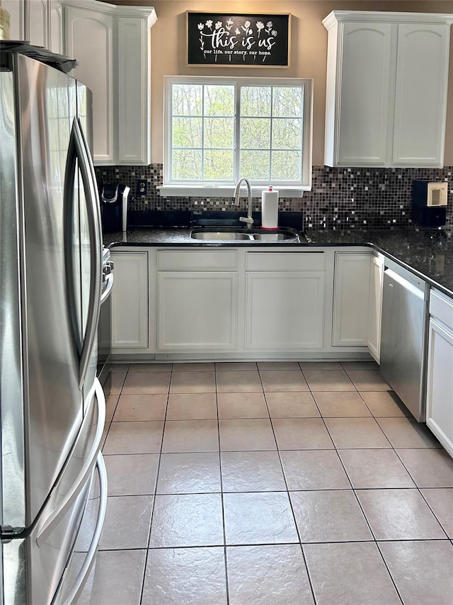 kitchen featuring light tile patterned floors, white cabinetry, a sink, stainless steel appliances, and backsplash