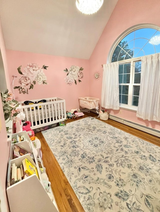 bedroom featuring lofted ceiling, wood finished floors, baseboard heating, and a crib