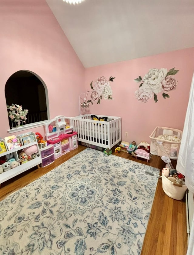 bedroom with wood finished floors, a nursery area, and vaulted ceiling