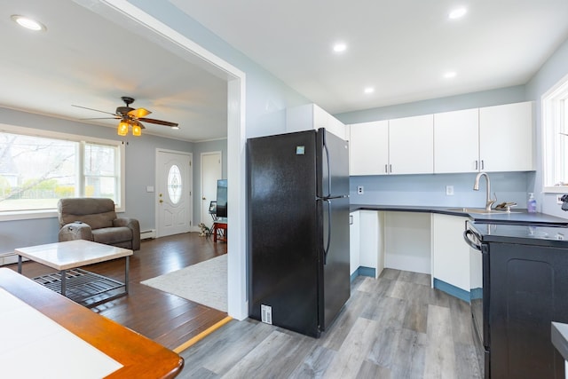 kitchen featuring a sink, black appliances, open floor plan, light wood-type flooring, and white cabinets
