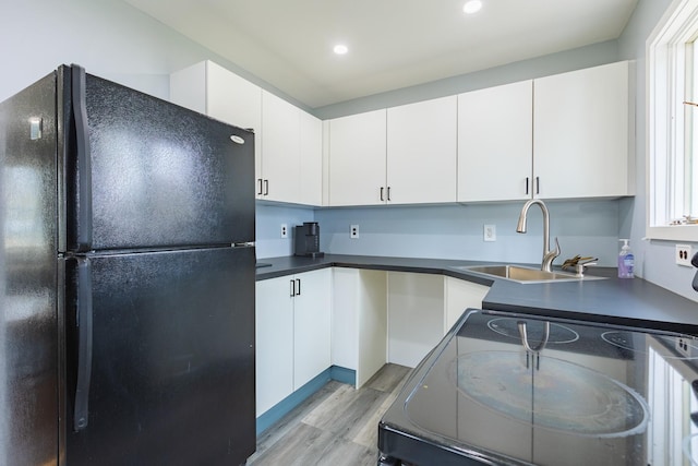kitchen with dark countertops, a sink, light wood-type flooring, black appliances, and white cabinetry