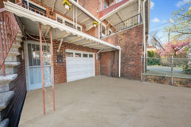 view of property exterior featuring brick siding, driveway, a balcony, and fence