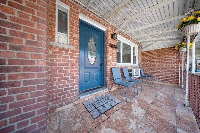 doorway to property featuring brick siding and a porch