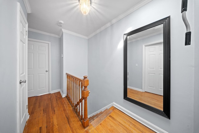 hall featuring wood finished floors, crown molding, baseboards, and an upstairs landing