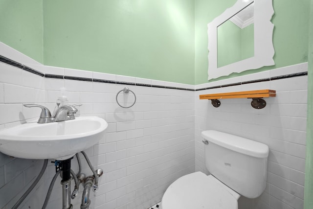 half bath featuring tile walls, a wainscoted wall, a sink, and toilet