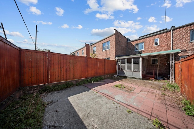 rear view of property featuring brick siding, a patio area, a sunroom, and a fenced backyard
