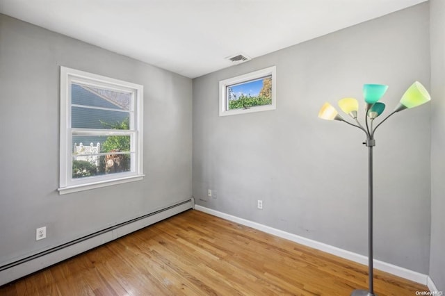 spare room with light wood-type flooring, visible vents, a baseboard heating unit, and baseboards